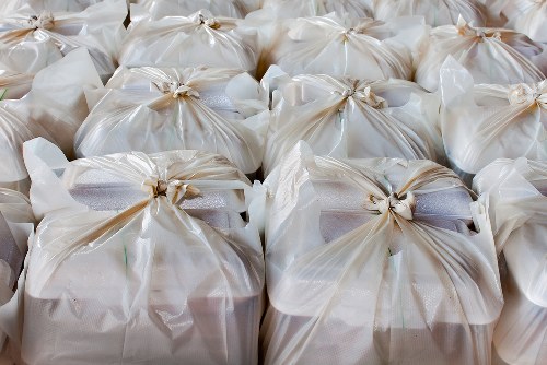 A close-up view of multiple large white plastic bags filled with waste, arranged in rows on a flat surface. The bags are tied at the top with knots, and the material appears to be smooth and glossy. The contents are not visible but the bags look full and are likely used for rubbish collection or disposal. The background shows more similar bags, with no specific environmental context visible, suggesting the scene could be outdoors or in a storage area. The lighting is even, highlighting the texture and sheen of the plastic. This image relates to rubbish removal services such as those offered by Office Clearance Kensington, which operates in areas including Kensington and the surrounding London boroughs, providing waste clearance for commercial or residential properties.